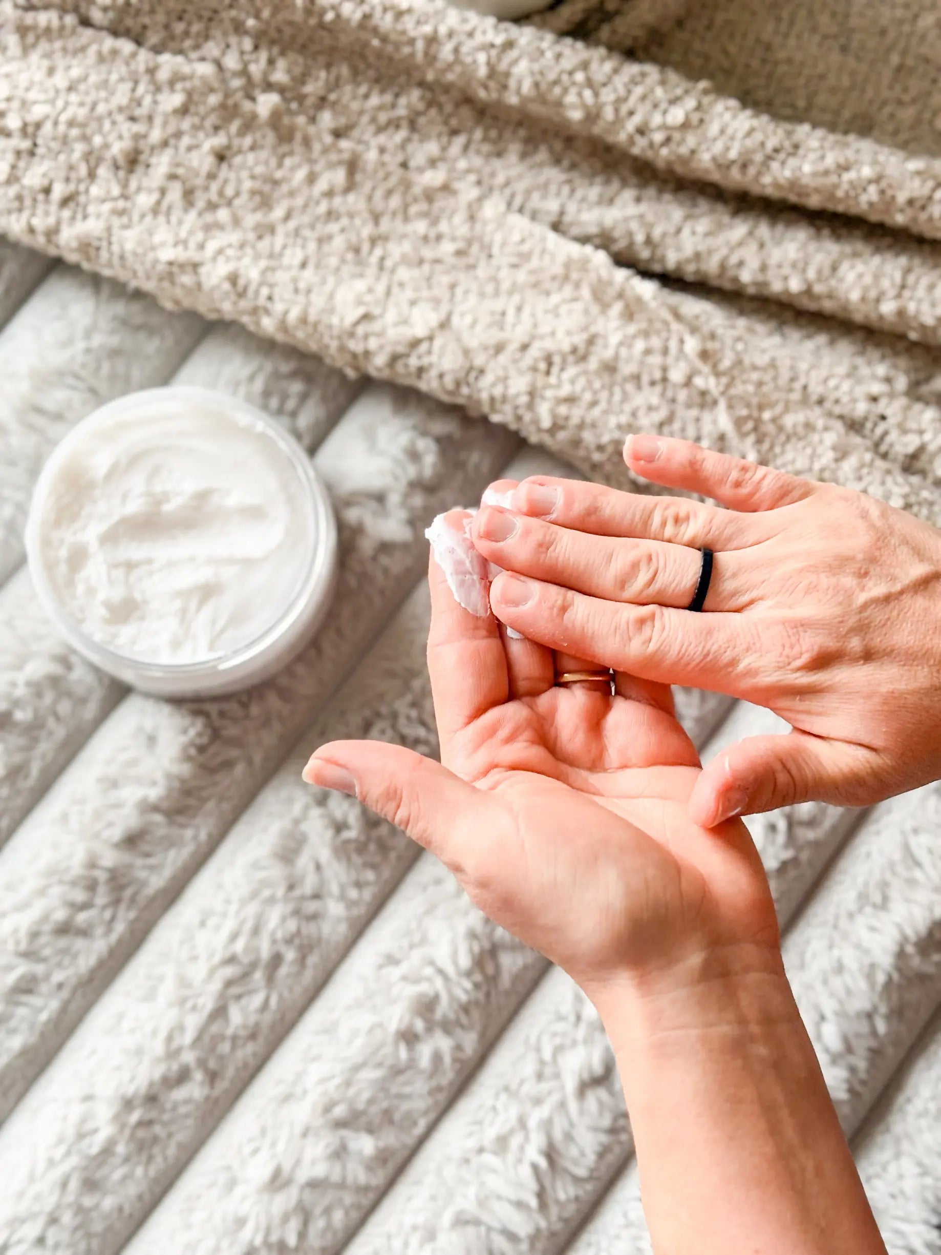 Moisturizing white cream in open jar being applied to a woman’s hand