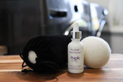 White bottle of purple duck laundry scent booster with a black drawstring bag and white ball on a wooden surface.