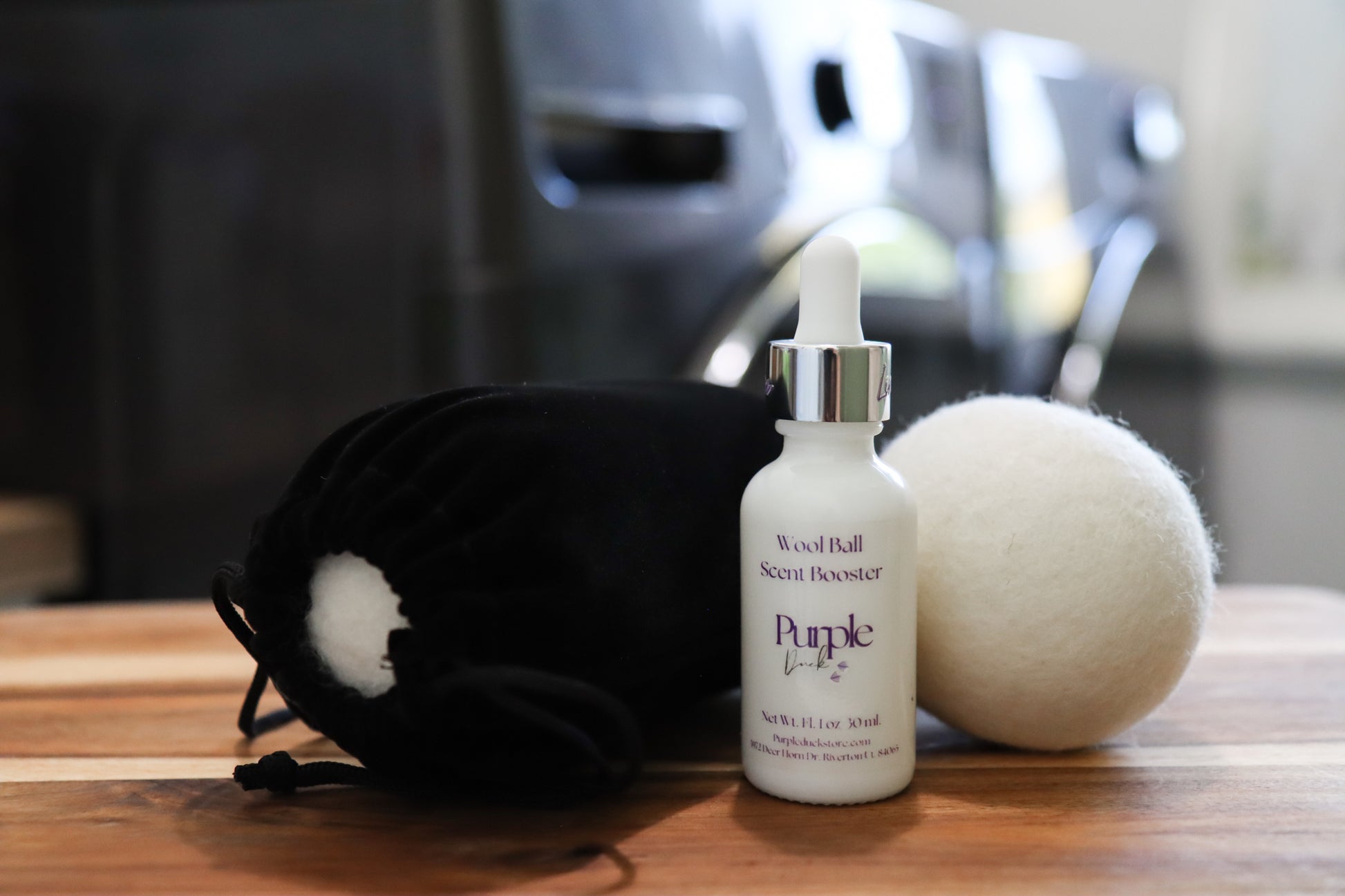 White bottle of purple duck laundry scent booster with a black drawstring bag and white ball on a wooden surface.