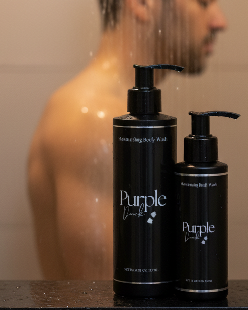 Man in a shower with two bottles of Purple Duck Body Wash on a counter.