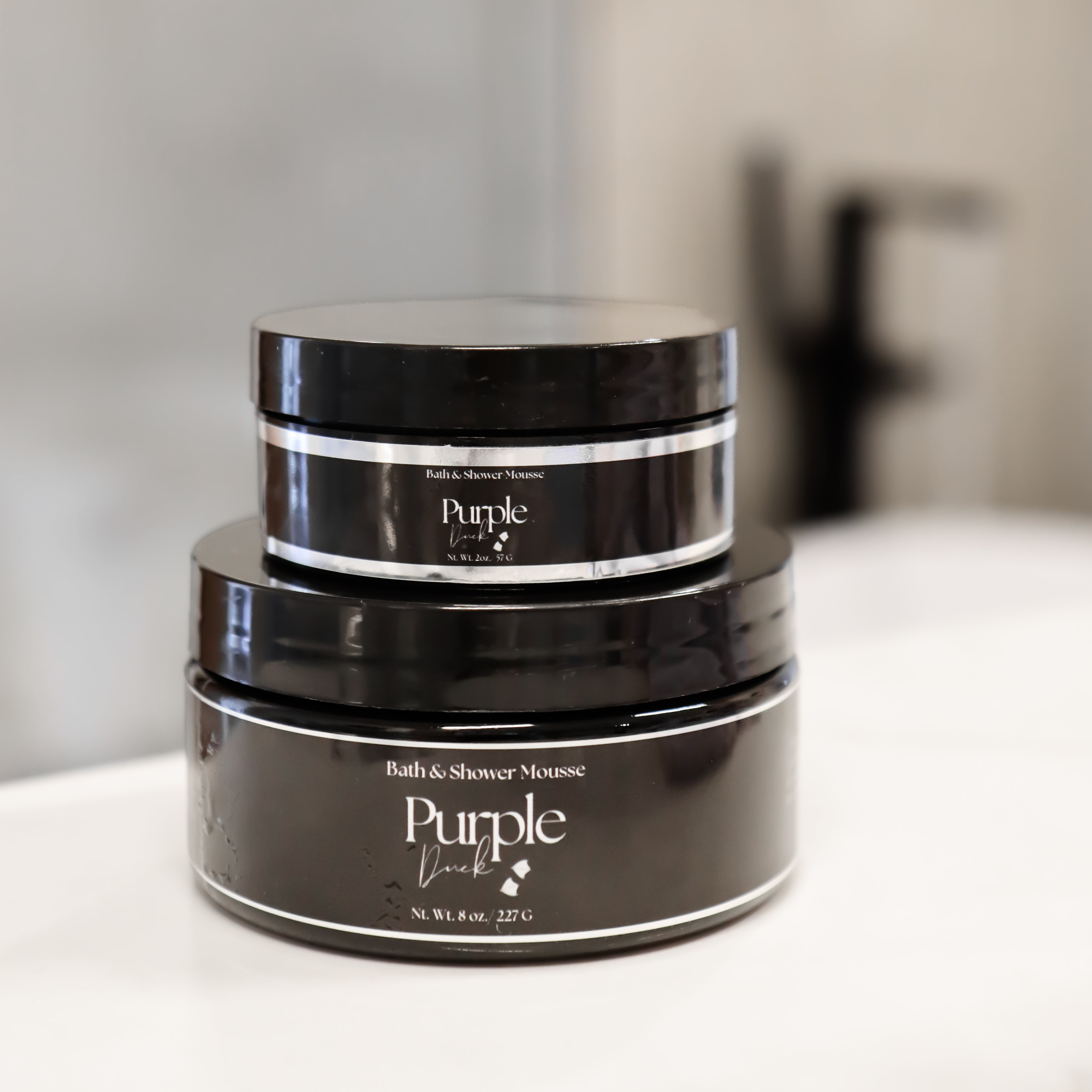 A stack of 2 oz and 8 oz Shower Mousse sitting on a bathroom counter