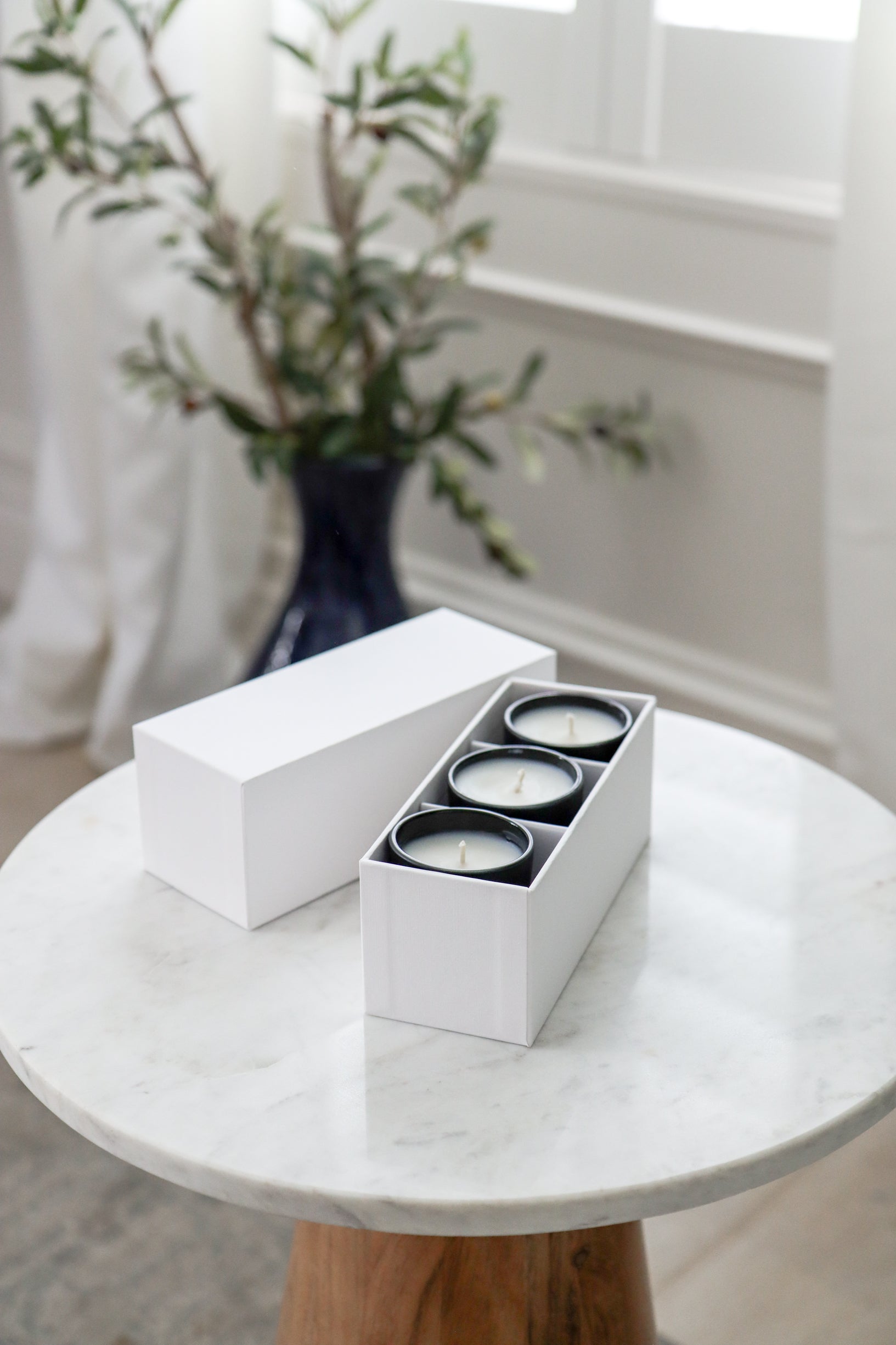 Three sample candles in a white box on a marble table with a vase of flowers in the background.