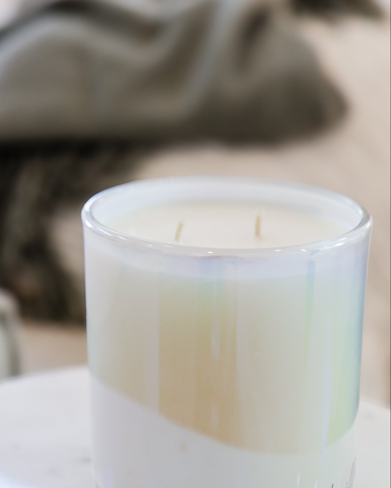 Candle in a glass container on a table with a blurred background showing a couch and plant.