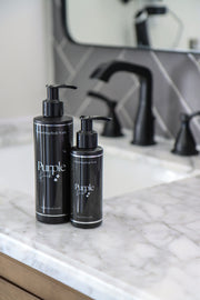 Two bottles of Purple Duck Men's Body Wash on a marble countertop with a blurred background