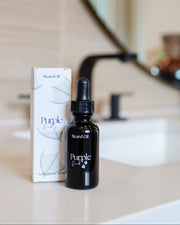 A bottle of Men's Natural Beard Oil with a dropper cap, displayed next to its packaging box on a bathroom counter.