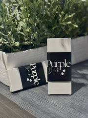 \Purple Duck Sample Cologne on a surface with green plants in the background